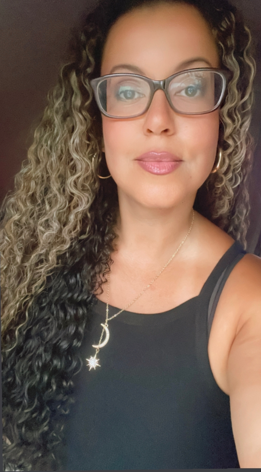 Lisa Latimer – Social Selling Sirens Founder Portrait Lisa Latimer, a woman with long curly hair and glasses, wearing a black top and crescent moon necklace.